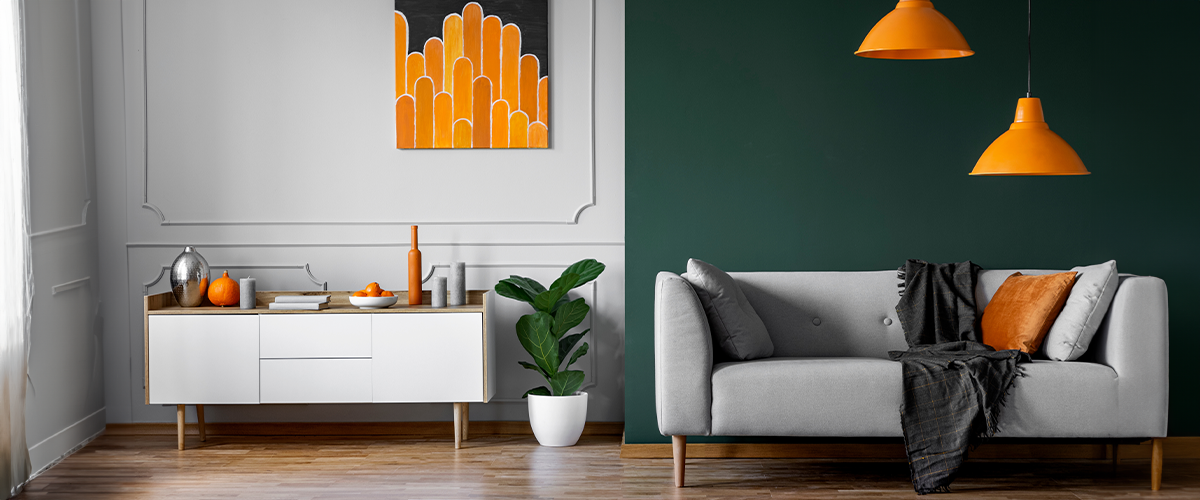 A stylish modern living room with a gray sofa, orange accents, and a dark green wall.