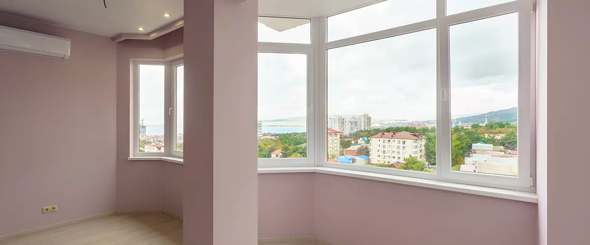 Freshly painted room with large windows offering a city view, showcasing pastel pink walls