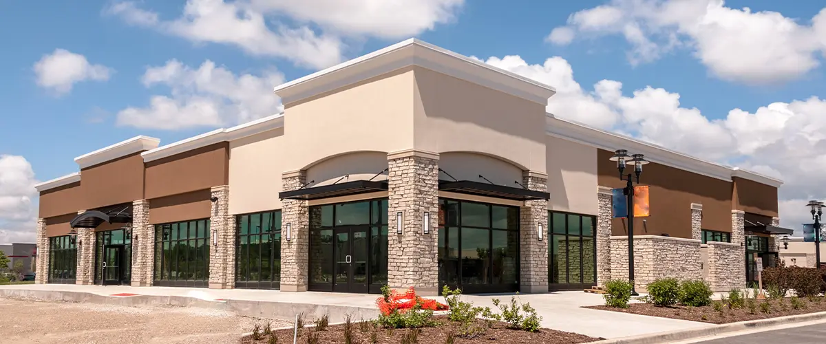 Newly constructed commercial building with a modern design, large glass windows, and stone accents under a clear blue sky.