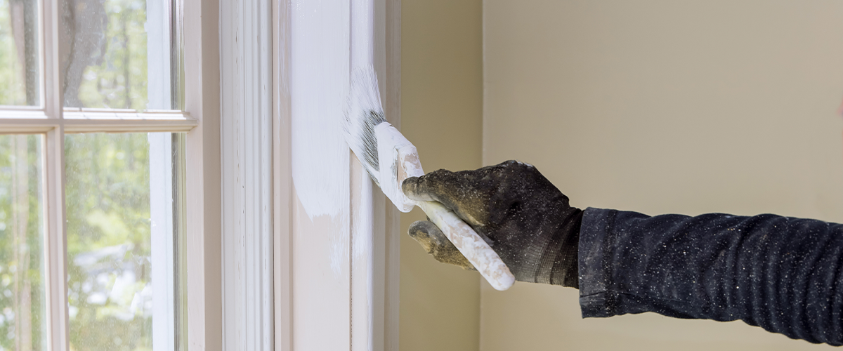 Painter wearing a black glove trim painting in Honolulu, using a brush, with sunlight streaming through the window.