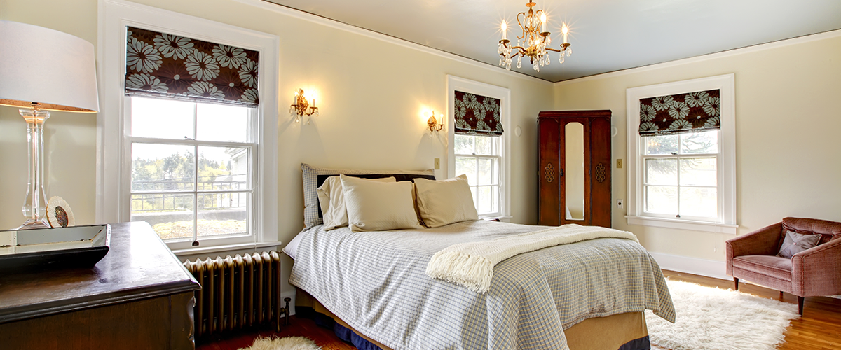 Spacious bedroom with elegant chandelier, large windows, patterned blinds, cozy bed, vintage wardrobe