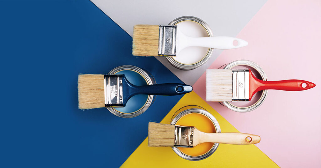 Various paint brushes rest on open paint cans filled with different colors on a multi-colored background.
