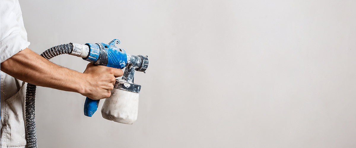 Worker holding a blue paint sprayer, applying a fresh coat of paint to an interior wall, showcasing home renovation and painting services.