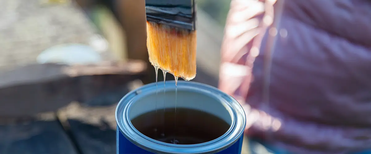 Close-up of a paintbrush dripping varnish over a can. The Difference Between Lacquer And Paint.