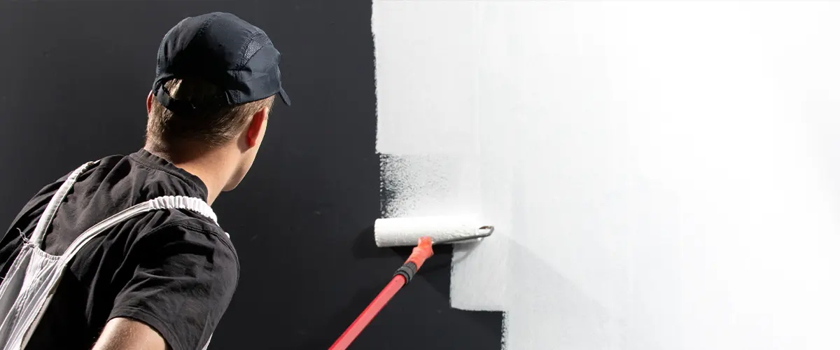 Painter using a roller to apply white paint over a dark wall, professional painting job with a smooth finish.