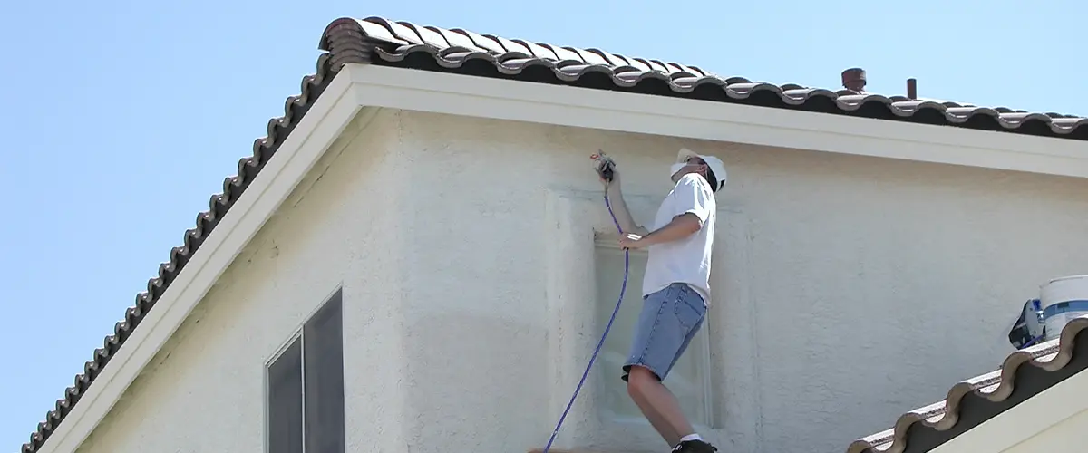 Exterior Painting Companies in Mililani, HI 2 Professional painter using a spray gun the exterior painting of a two-story house in Mililani, on a high platform.