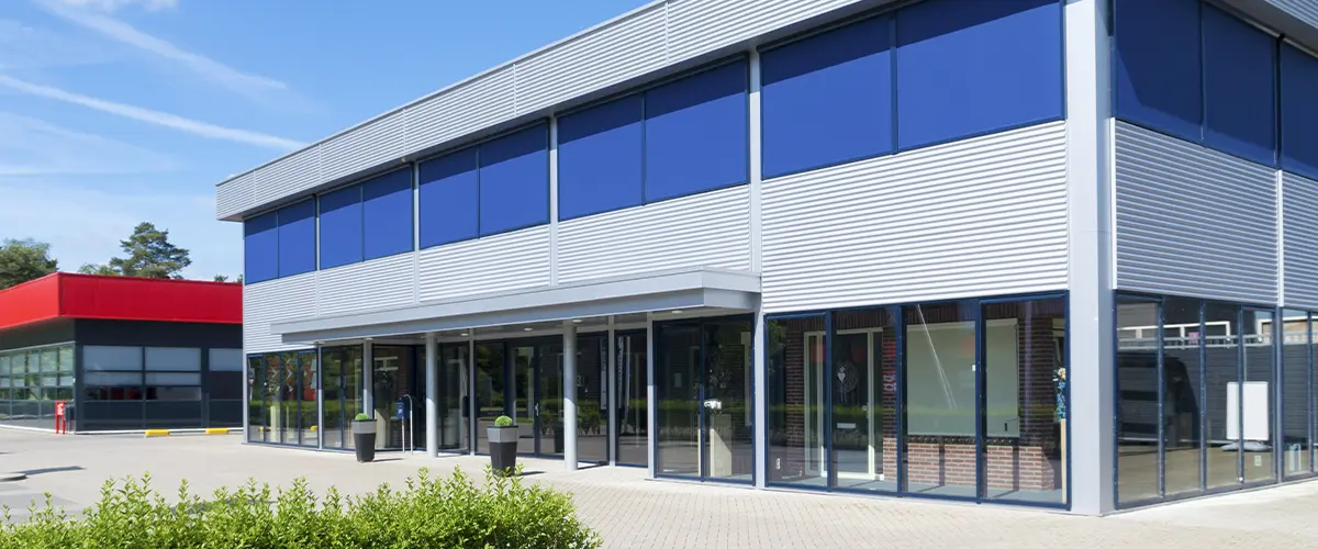 Modern commercial building exterior with blue window shades and large glass entrance under a clear sky.