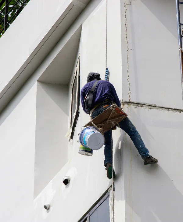 A professional painter working on the exterior of a tall building using safety harnesses.