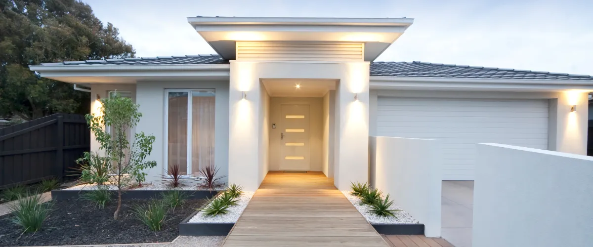 A modern house exterior with minimalist landscaping and warm exterior lighting.