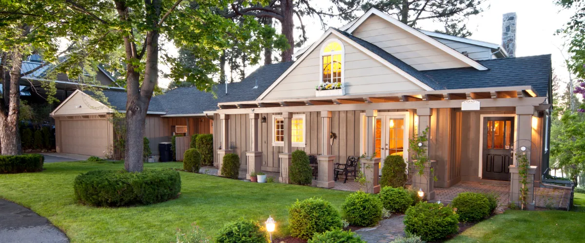 A cozy traditional home with a front porch, garden, and elegant exterior lighting.