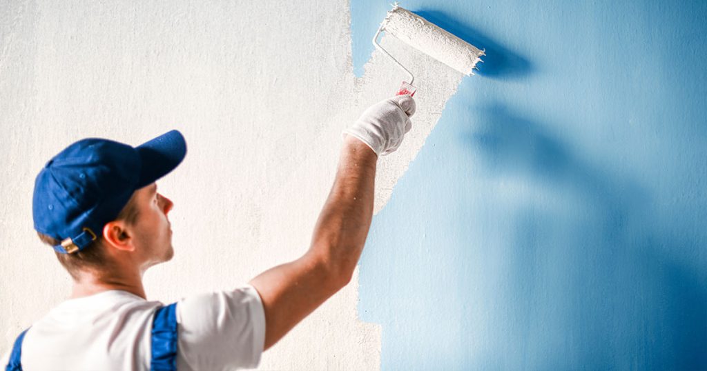 How Often Should You Repaint Your Home’s Interior in Waipahu? 5 Professional painter using roller to apply white paint over blue interior wall during house painting project