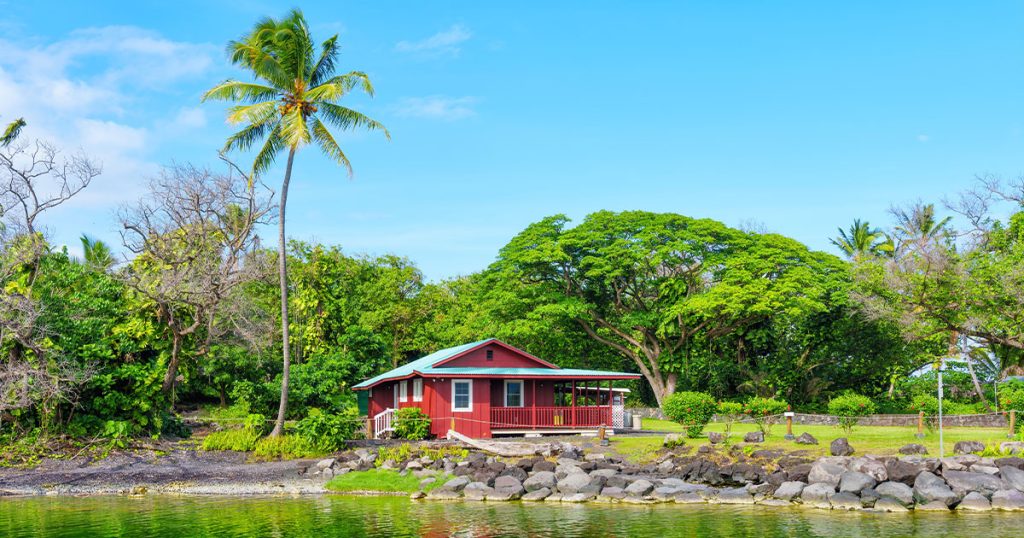 The Best Paint Colors for Homes in Honolulu: Stay Cool & Stylish 7 Red Hawaiian beachfront cabin with green roof, lush tropical trees, and rocky shoreline by calm ocean water