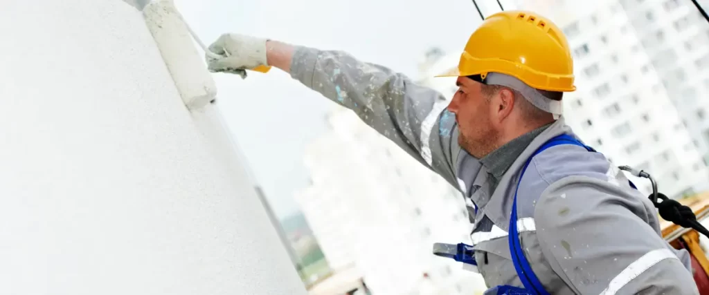 Why Commercial Buildings in Honolulu Need Special Paint Coatings 2 Construction worker painting exterior wall with a roller