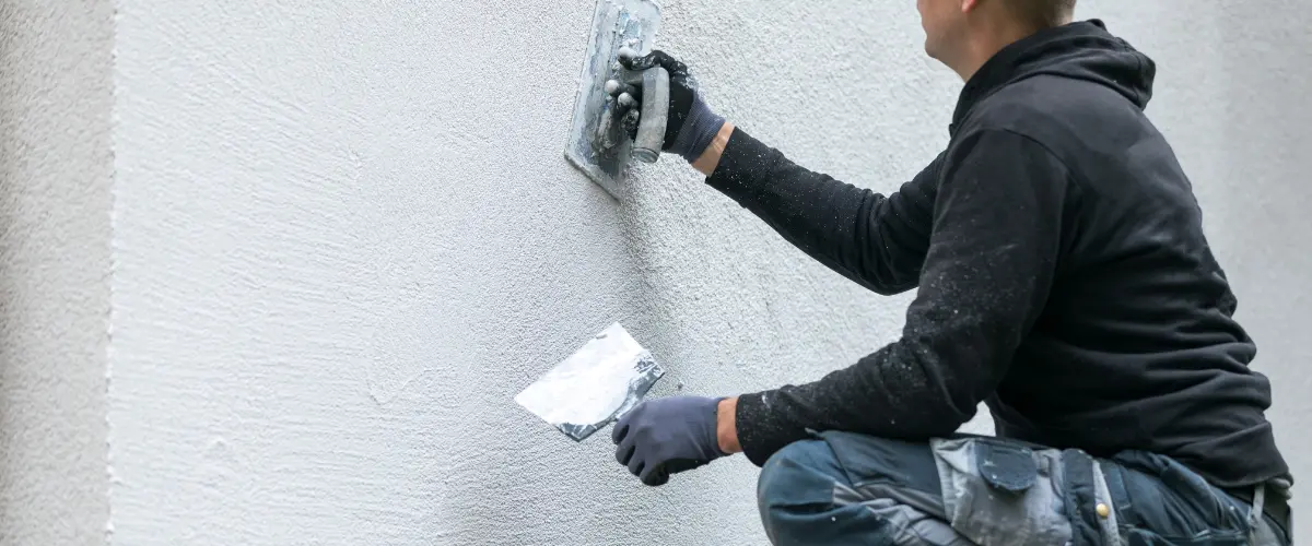 Contractor applying stucco to exterior wall with a trowel