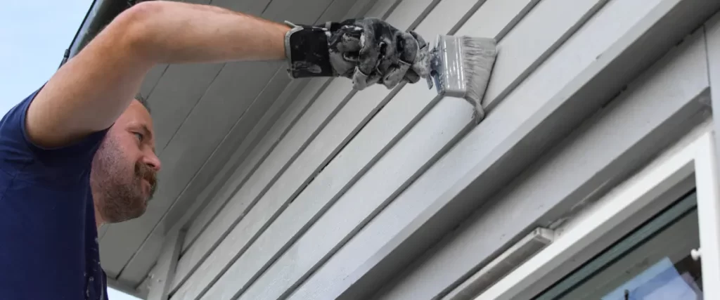 Gloved hand painting siding with a brush