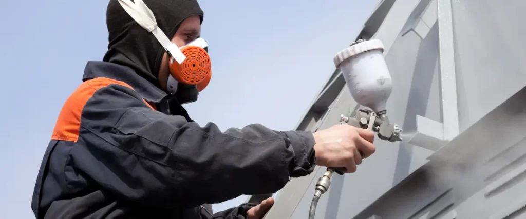 Worker wearing a respirator mask using a spray gun for exterior painting