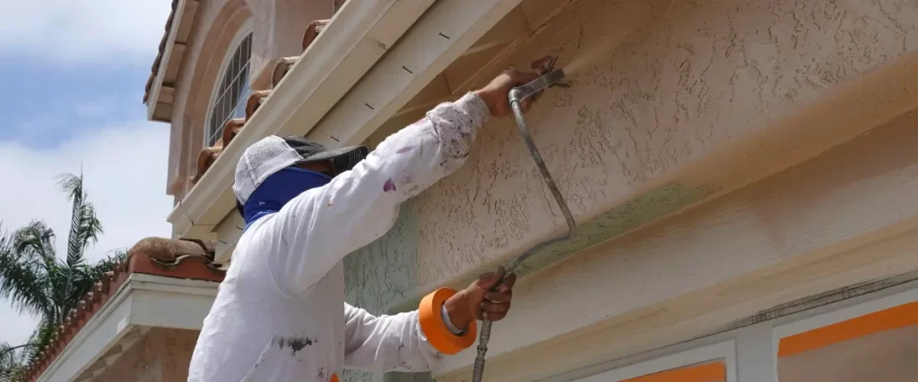 Bamboo, Lava Rock & Stucco: Painting Hawaii’s Unique Home Exteriors 1 Worker using a roller to paint the soffit and stucco exterior of a house
