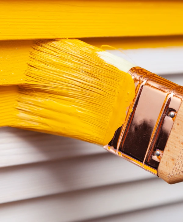 Top 10 Exterior Painting Companies In Wahiawa, HI 1 Close-up of a paintbrush applying bright yellow paint to exterior siding