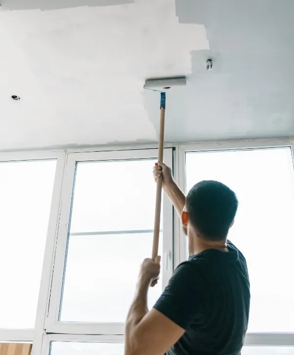 A man painting the ceiling with a brush, standing on a ladder, focused on his task