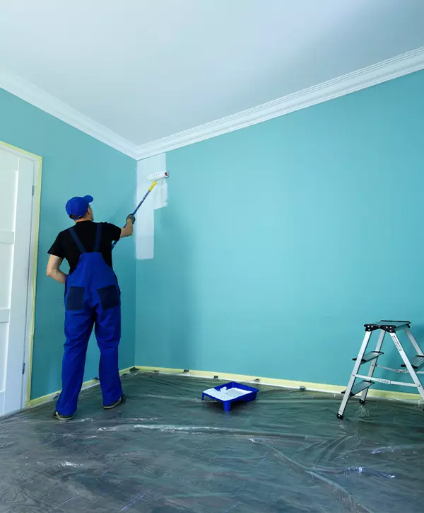 Top Interior Painting Companies In Pearl City, HI 1 Experienced interior painter in blue overalls working on a light blue wall in a Pearl City home, demonstrating professional prep work.