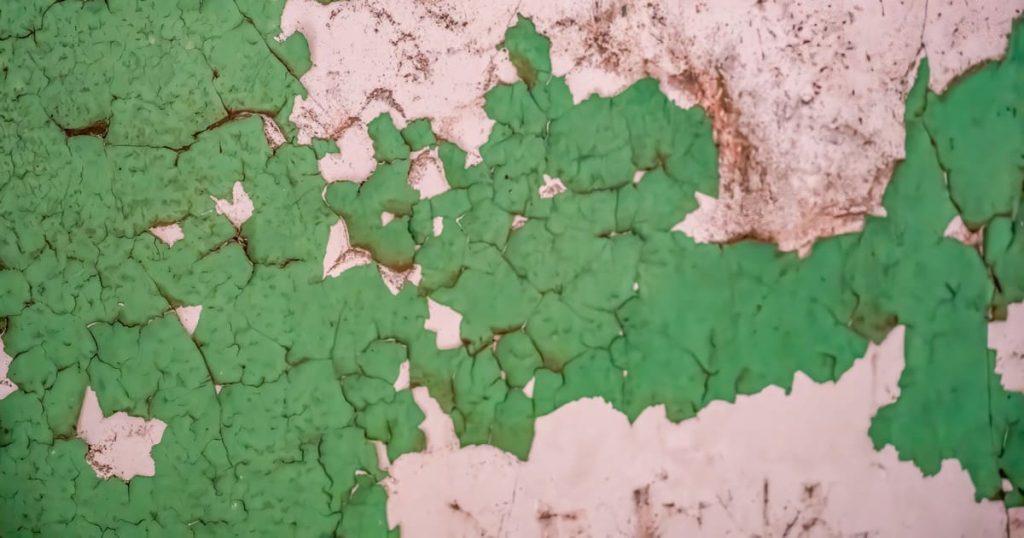Lead Abatement in Oahu: When Is It Required? 1 Layers of old green paint cracking and flaking off a white wall in large chunks, requiring expert lead abatement in Oahu to ensure safety.