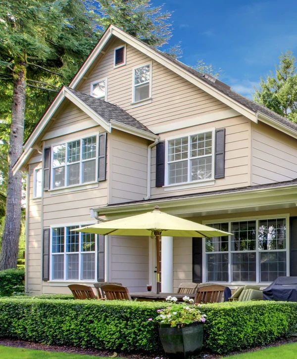 A beautifully updated beige two-story home with dark shutters and a patio umbrella, showcasing fresh exterior painting in Aiea, HI.