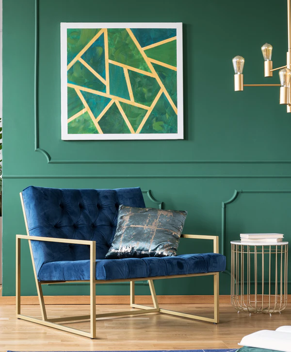 A plush blue velvet armchair with a gold frame set against a deep emerald green wall featuring decorative molding, showcasing expert interior painting in Aiea, HI.